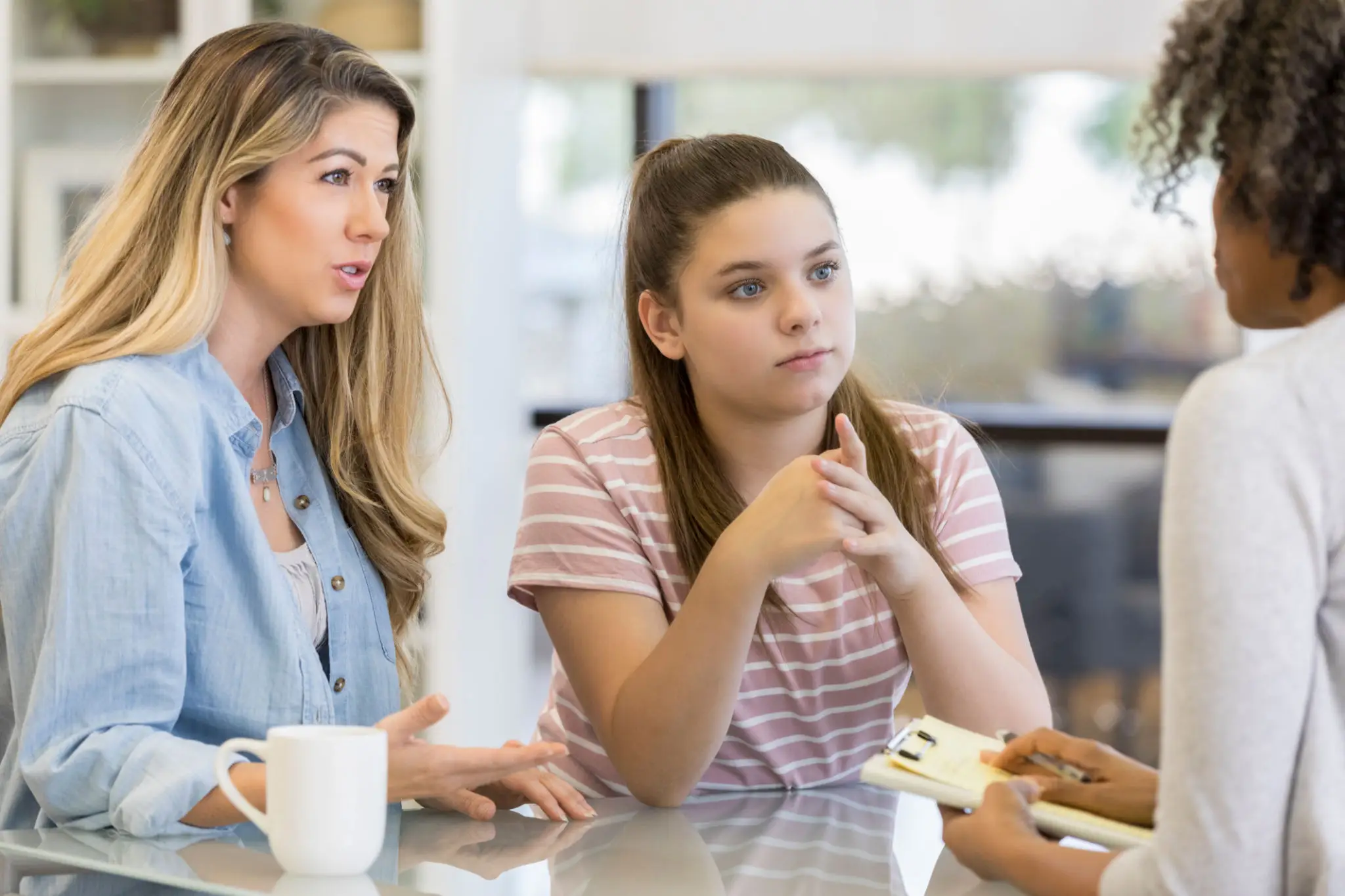 A mother and daughter having a serious conversation at a kitchen table.